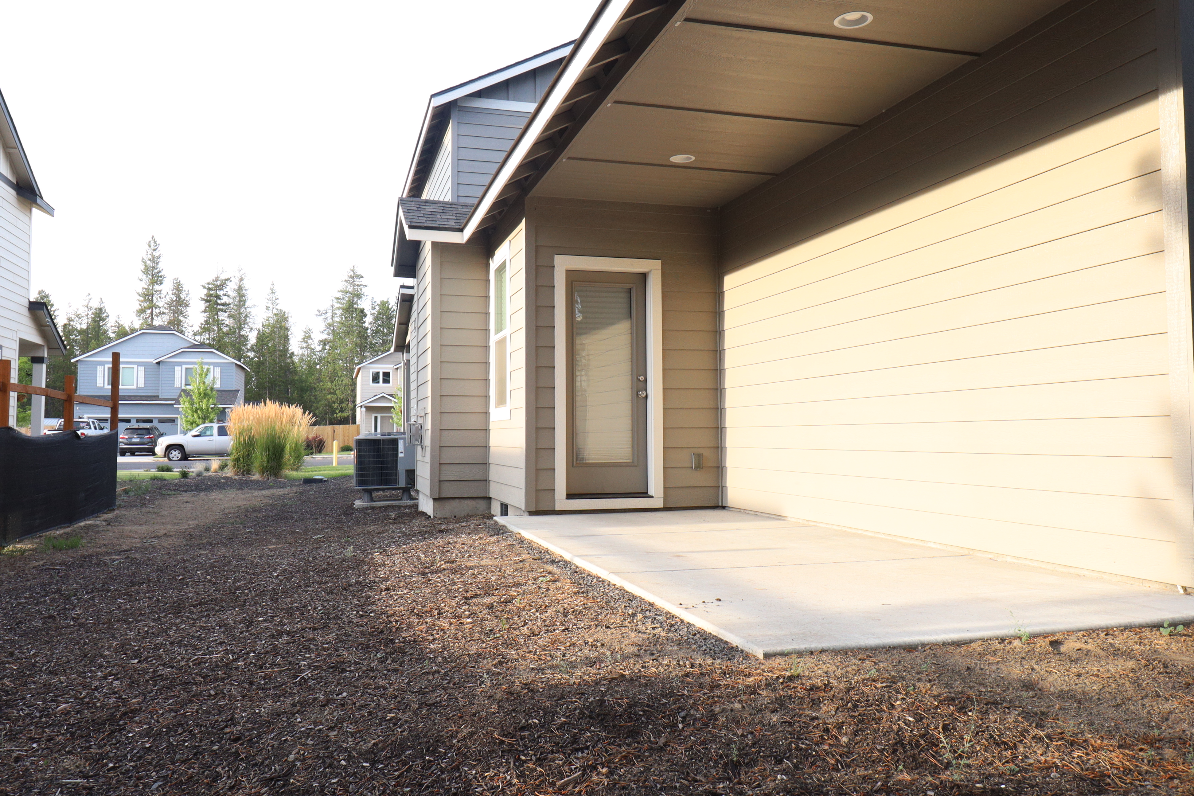 Covered side entry and gravel side yard with a concrete pad beside the attached two-car garage