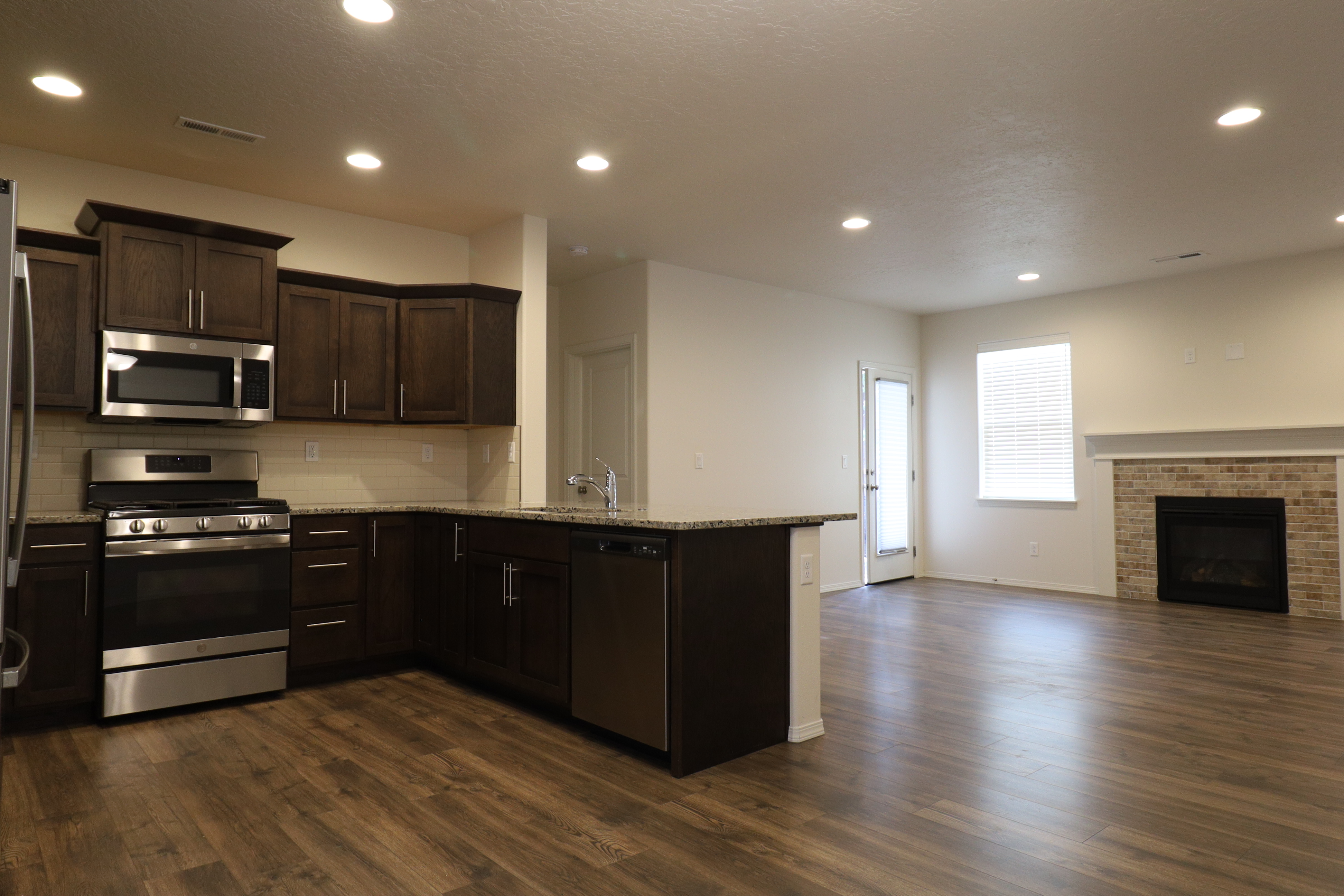 Open kitchen and living room with laminate flooring, granite counter seating and a gas fireplace