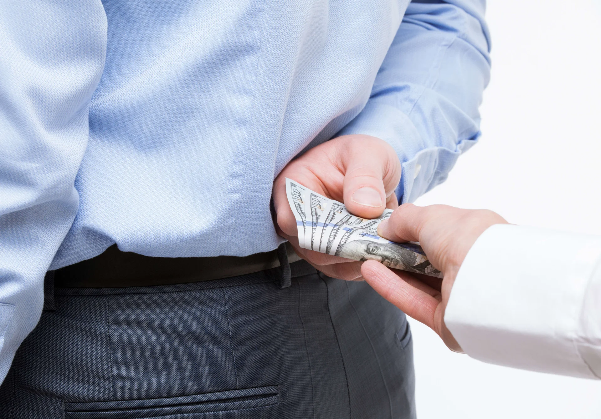Business man handing off cash behind his back to someone behind him as a referral fee Business man handing off cash behind his back to someone behind him as a referral fee